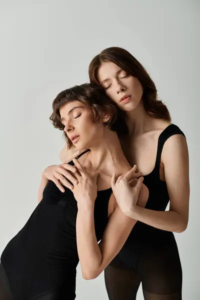 Zwei junge Frauen in schwarzen Leibchen umarmen sich mit geschlossenen Augen vor grauem Hintergrund. — Stockfoto