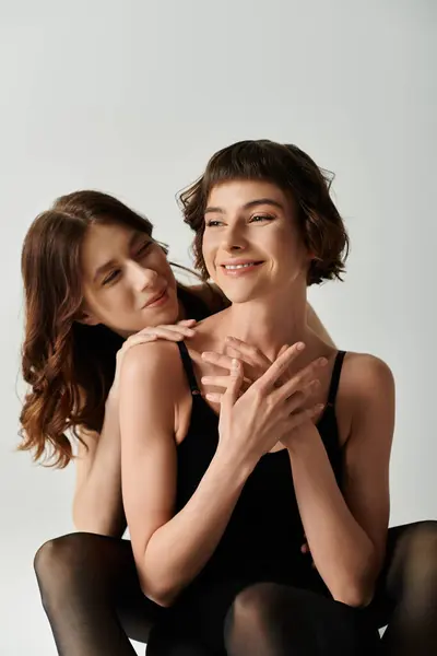 Pareja joven lesbiana en trajes negros posan sobre fondo gris. lgbt amor — Stock Photo