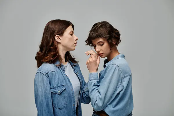 Two stylish women in denim shirts pose against a grey backdrop. — Stock Photo
