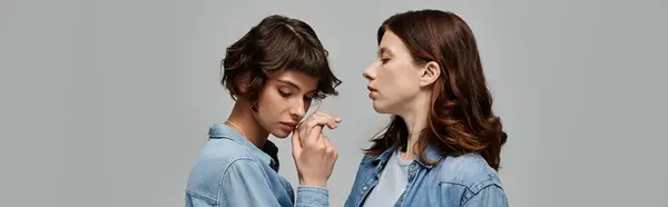 Two young women in denim attire pose against a grey background, showcasing their stylish fashion choices. — Stock Photo