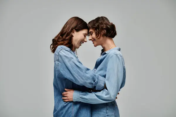 Two young women, in denim attire, embracing in front of a gray background. Lesbian couple — Stock Photo