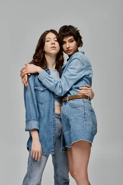 Two women in denim are embracing against a grey background, capturing a romantic and stylish moment. — Stock Photo