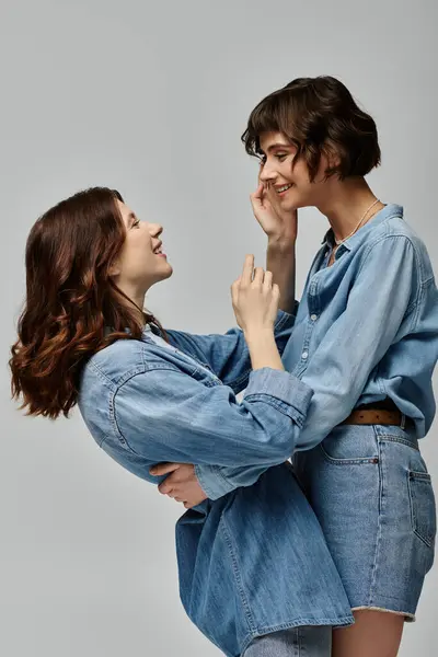 Two trendy young women in denim attire striking a pose side by side against a gray background. — Stock Photo