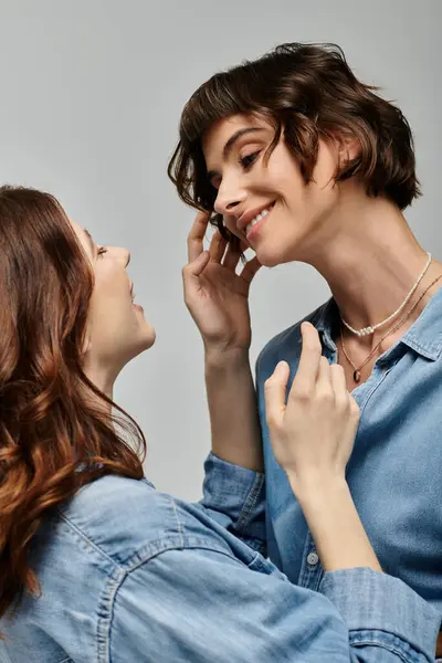Two young women in denim shirts pose against a grey background, their eyes locked in a shared moment of affection. — Stock Photo