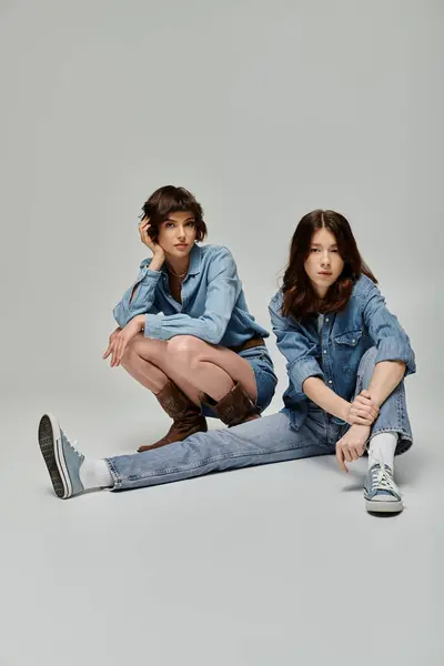 Due giovani donne in abiti in denim posano su uno sfondo grigio, in mostra una coppia lesbica alla moda. — Foto stock