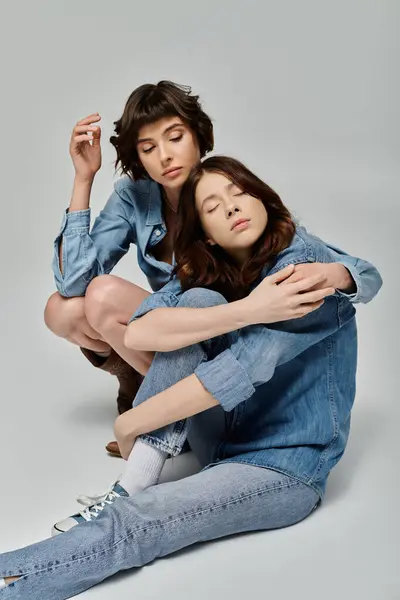 A young lesbian couple in stylish denim attire poses against a grey background. — Stock Photo