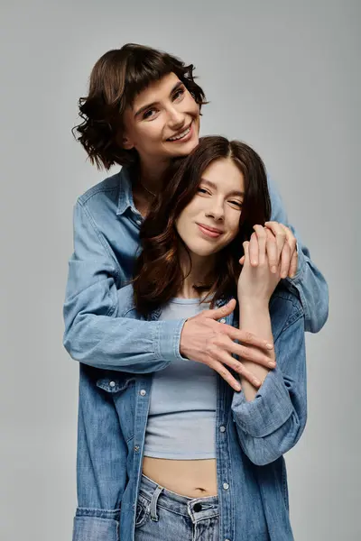 Una elegante pareja lesbiana vestida de mezclilla posa para un retrato sobre un fondo gris. - foto de stock