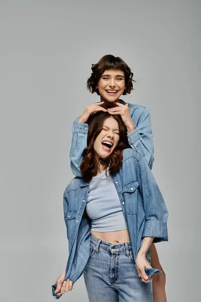 Two stylish young women in denim attire pose playfully against a grey background. — Stock Photo