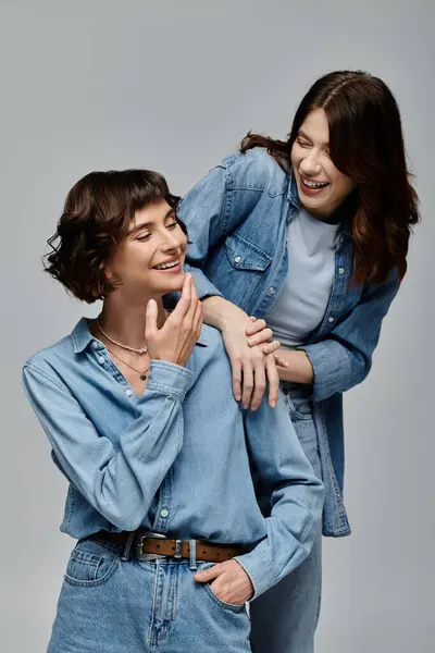 Two stylish young women in denim attire pose against a grey background, laughing and looking happy together. — Stock Photo