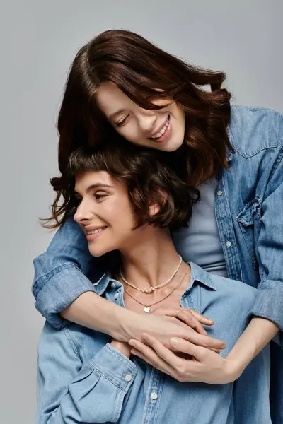A stylish lesbian couple, both wearing denim shirts, pose together and smiling on a grey background. — Stock Photo