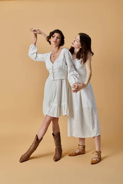 Young women in chic white dresses, capturing fashion and love in a light-hearted romantic scene against a beige backdrop. — Stock Photo