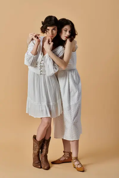 Two young women in white summer dresses stand close together on a beige background. Lesbian couple — Stock Photo