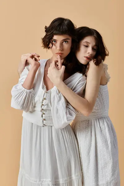 Two young women wearing white summer dresses embrace against a beige backdrop. Lesbian couple — Stock Photo