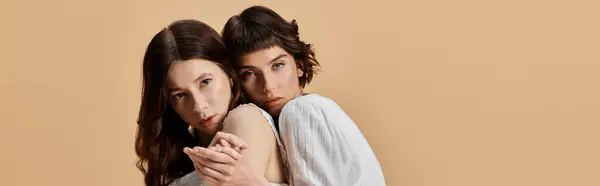 Duas mulheres jovens em vestidos de verão brancos posam juntas contra um fundo bege. — Fotografia de Stock