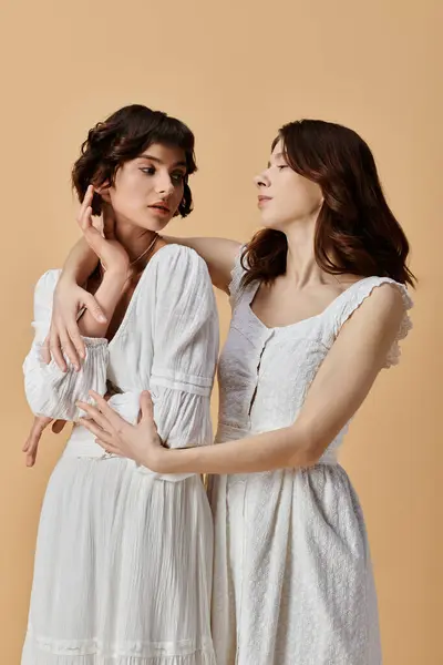 Two young women in white summer dresses pose against a beige background, showcasing a romantic and stylish lesbian couple. — Stock Photo