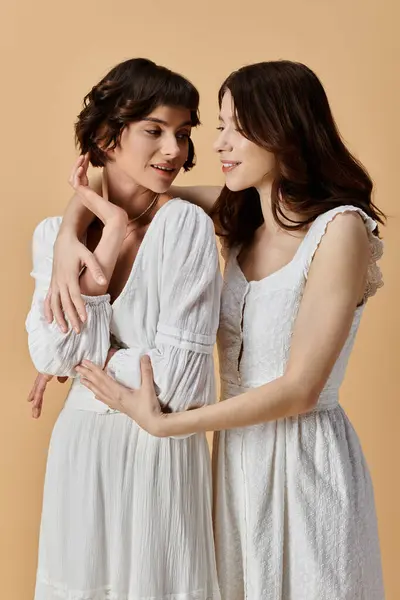Two stylish young women, dressed in white summer dresses, stand close together against a beige background. — Stock Photo
