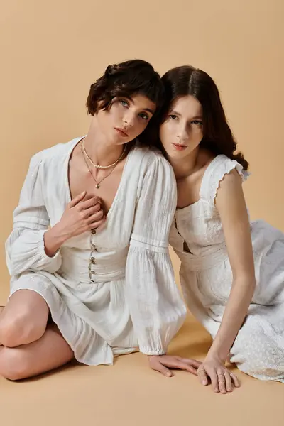 Two young women in white summer dresses pose against a beige background. Lesbian couple — Stock Photo