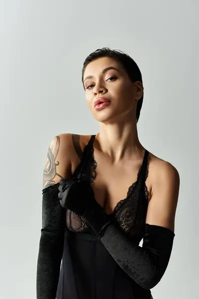 A young woman poses in black lingerie and gloves, with a confident and alluring expression. — Stock Photo