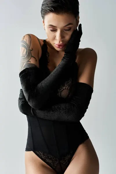 Una giovane donna in lingerie nera e guanti lunghi posa davanti a un muro bianco. — Foto stock