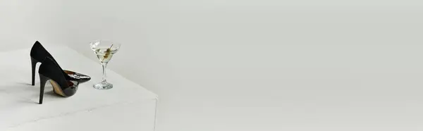 Two black high heels and a martini glass sit on a white surface. — Stock Photo