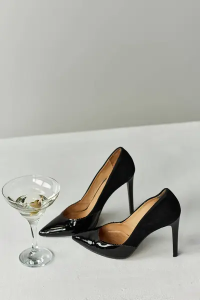 Two black high heels and a martini glass on a white surface. — Stock Photo