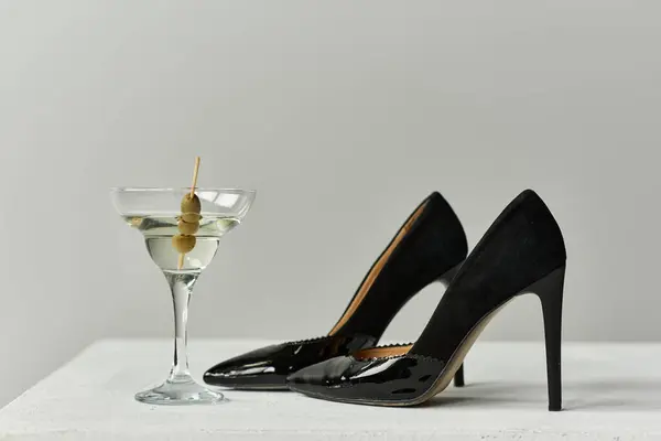 Two black high heels and a martini glass with olives on a white surface. — Stock Photo