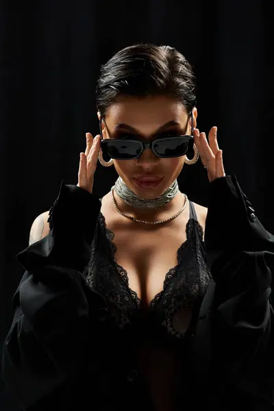 A young woman poses in black lingerie and sunglasses, looking mysterious and alluring. — Stock Photo