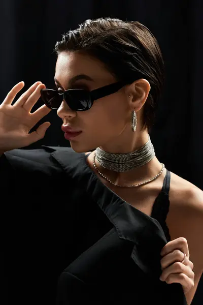 A young woman with short hair wearing black sunglasses and a black lingerie top poses confidently. — Stock Photo