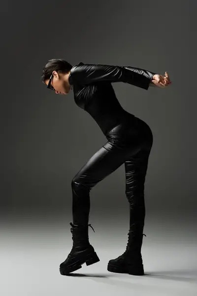 Femme dans une combinaison en cuir noir frappe une pose séduisante, jetant une longue ombre. — Photo de stock