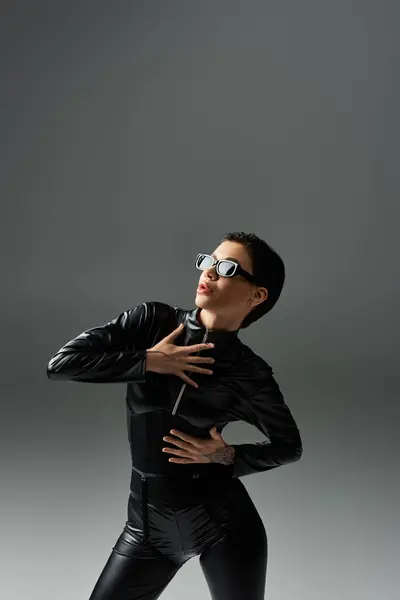 A woman in black leather jumpsuit poses against a grey backdrop. — Stock Photo