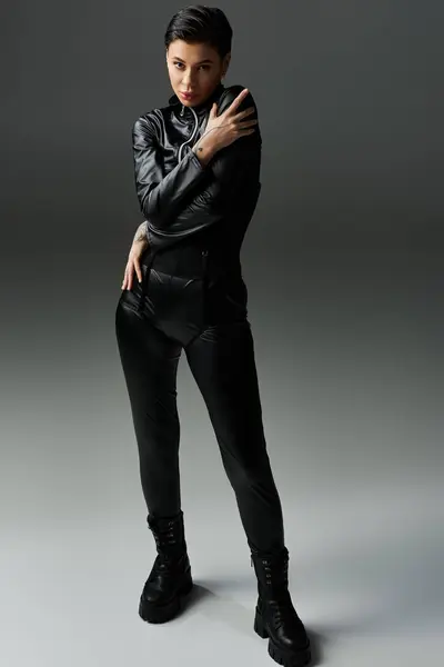 A woman in black leather poses with confidence against a gray backdrop. — Stock Photo