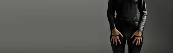 A woman in black jumpsuit stands against a grey background, posing with her hands on her hips. — Stock Photo