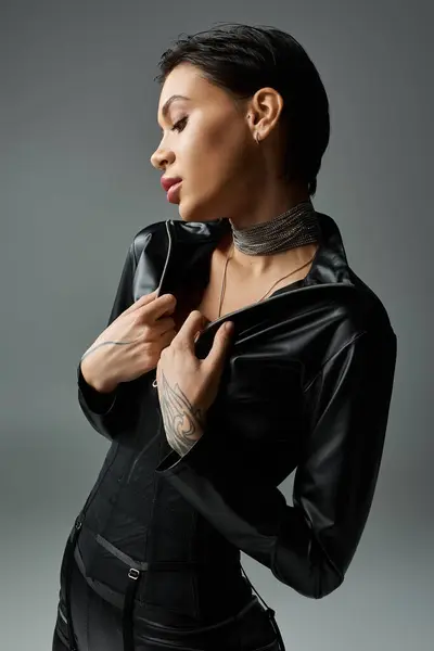 A woman in black leather jumpsuit poses seductively against a gray background. — Stock Photo
