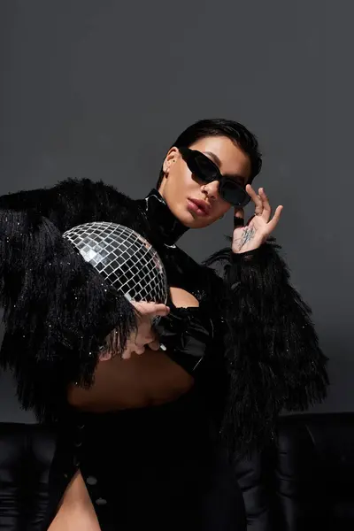 Una mujer vestida de negro sexy posa con una bola disco. - foto de stock