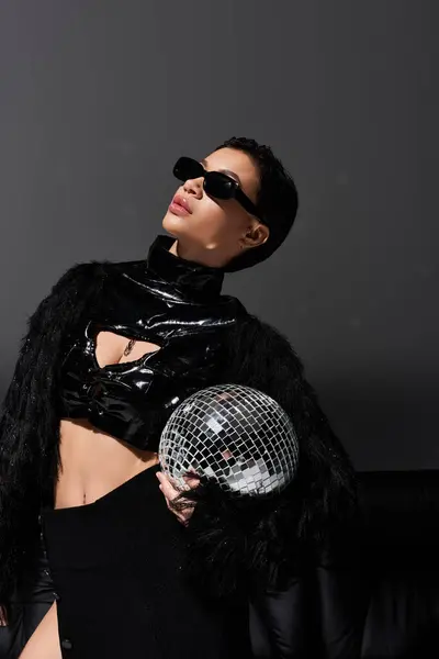 A woman in black sexy attire poses with a mirror ball in a dimly lit studio. — Stock Photo