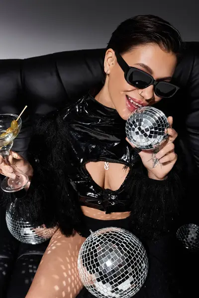Une femme en tenue sexy noire tient une boule disco et un verre de martini. — Photo de stock