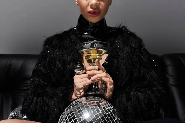 Uma mulher de traje sexy segura um copo de martini enquanto posando com uma bola de discoteca. — Fotografia de Stock