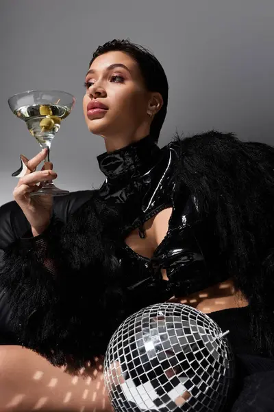 A young woman wearing sexy attire poses confidently with a martini and a disco ball. — Stock Photo
