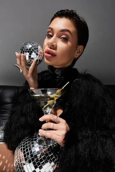 Una mujer en traje sexy posa con una bola de discoteca y una copa de martini. — Stock Photo