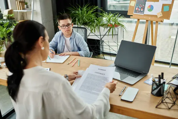 Une mère travaille sur des documents dans un bureau de son bureau pendant que son fils trisomique est assis à côté d'elle, dessinant. — Photo de stock