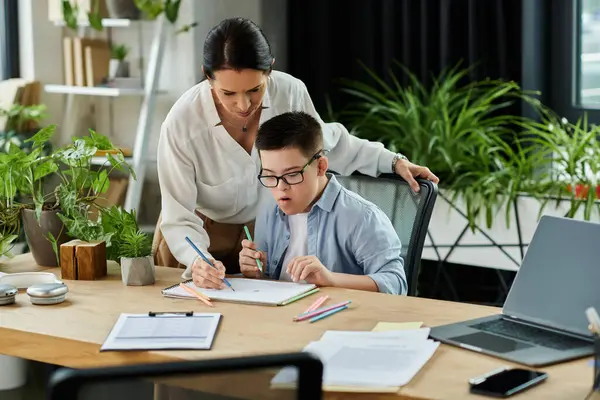 A mother helps her son with Down syndrome with his schoolwork in a home office setting. — Stock Photo