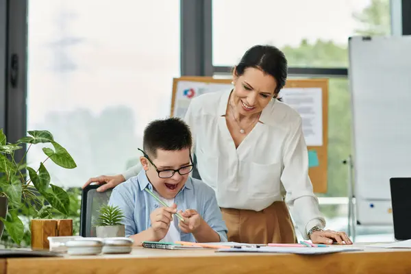 Una madre trabaja junto a su hijo con síndrome de Down en un entorno de oficina, destacando la inclusión y la diversidad. - foto de stock