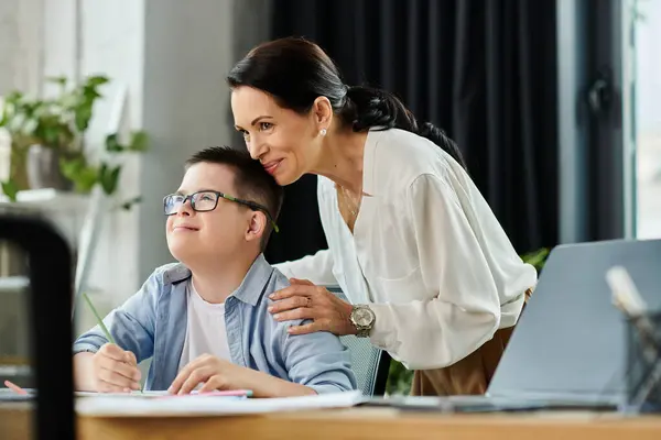 A mother works in her office while her son with Down syndrome sits beside her, demonstrating support and inclusivity. — Stock Photo