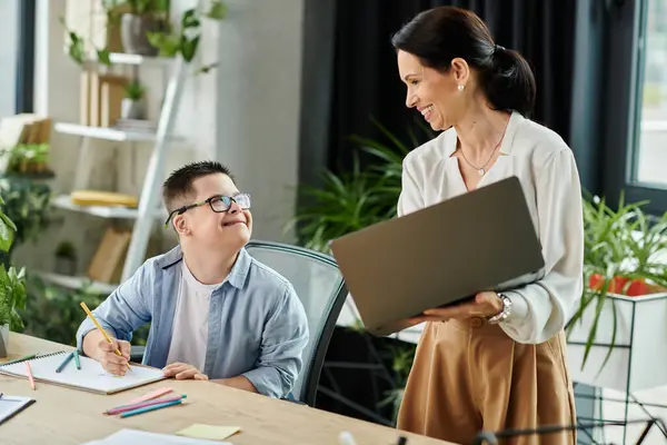 A mother smiles at her son as he works on a drawing at the office, demonstrating inclusivity and diversity in the workplace. — Stock Photo