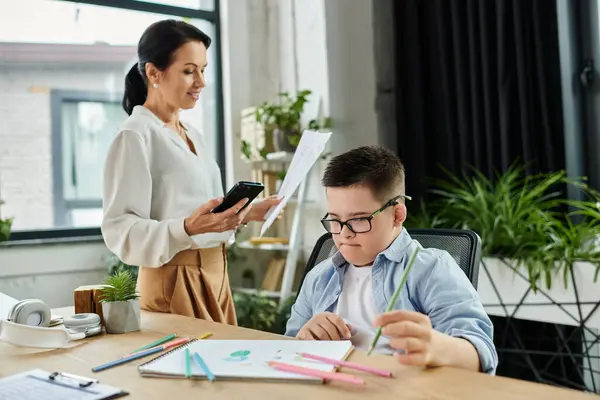 A mother works in her office while her son with Down syndrome colors at the table. — Stock Photo