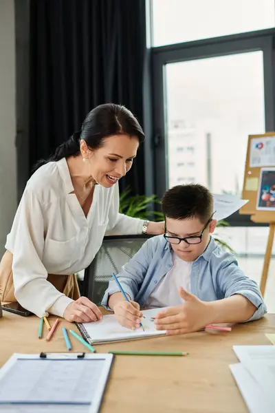 A mother helps her son with Down syndrome with his schoolwork at their home office. — Stock Photo