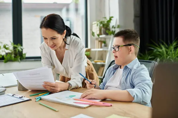 A mother works at her desk while assisting her son, who has Down syndrome, with a coloring activity. — Stock Photo