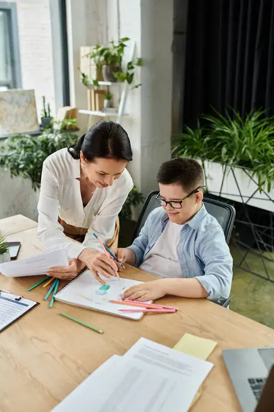 A mother and son with Down syndrome are drawing together in a modern office, showcasing inclusivity and diversity in the workplace. — Stock Photo