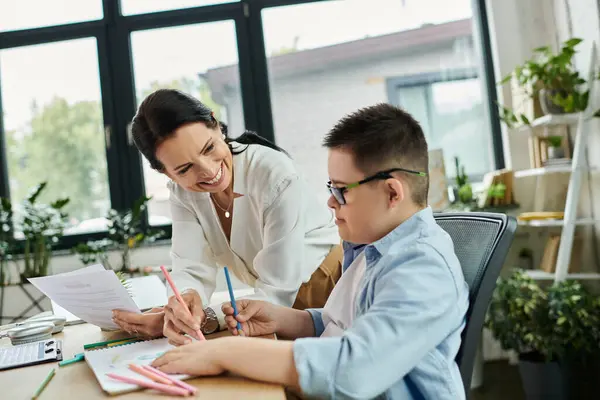 A mother smiles as she helps her son with Down syndrome color in a drawing at their home office. — Stock Photo