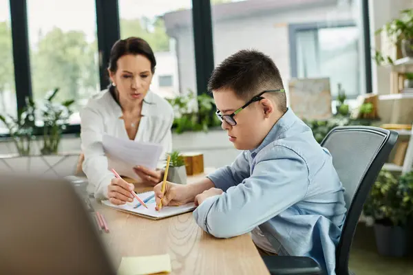 A mother works at her desk while her son colors nearby, both with focused expressions, showing an inclusive and loving environment. — Stock Photo